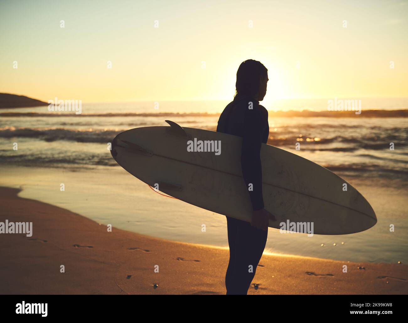 Attendre que les vagues parfaites se brisent. Vue arrière d'un jeune homme portant une planche de surf à la plage. Banque D'Images