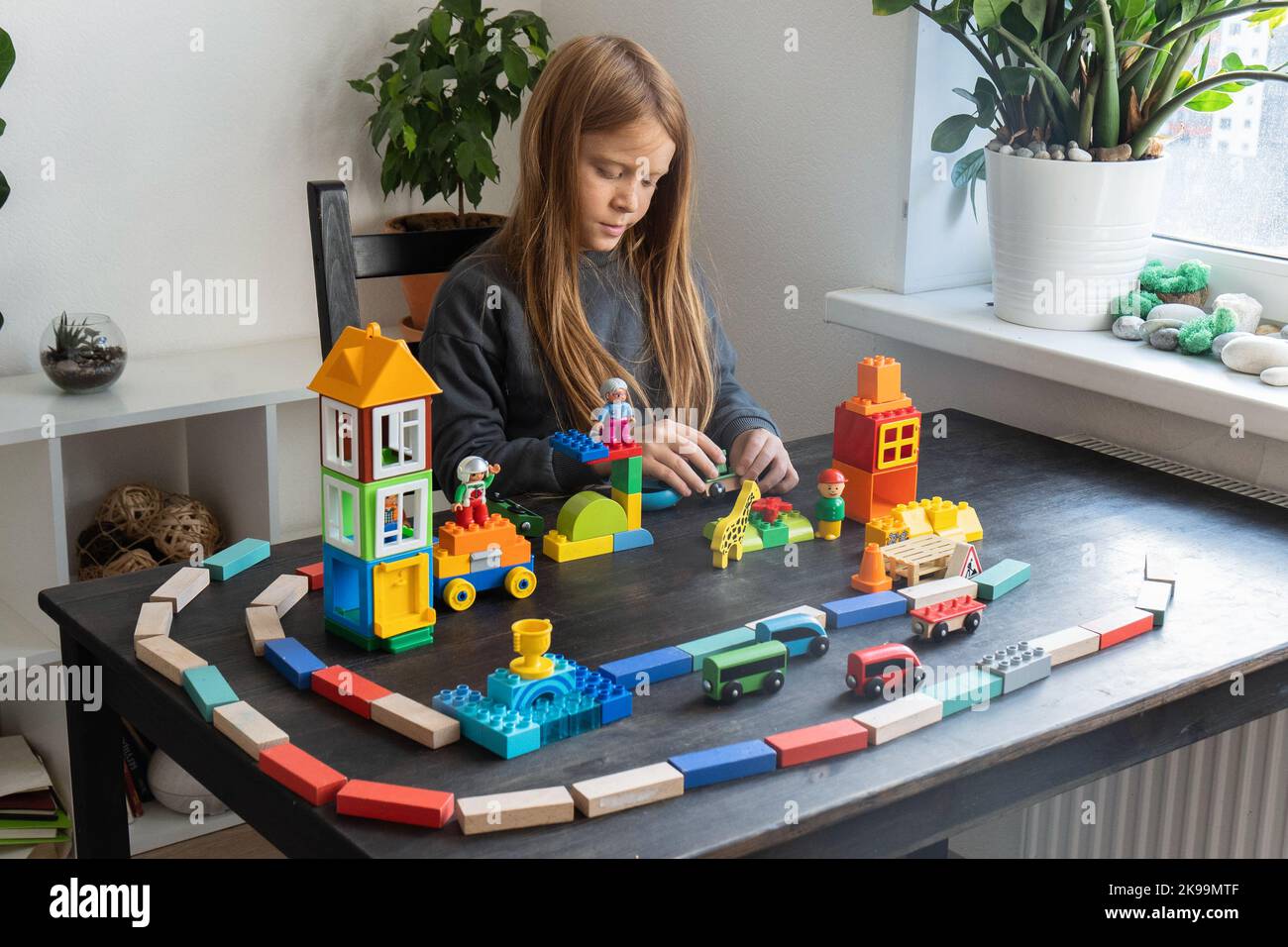 Le garçon de 8 ans joue des cubes et des blocs . Il a construit une ville et un chemin de fer. Activités de loisirs et loisirs à la maison. Un petit inventeur. Photo horizontale. Banque D'Images