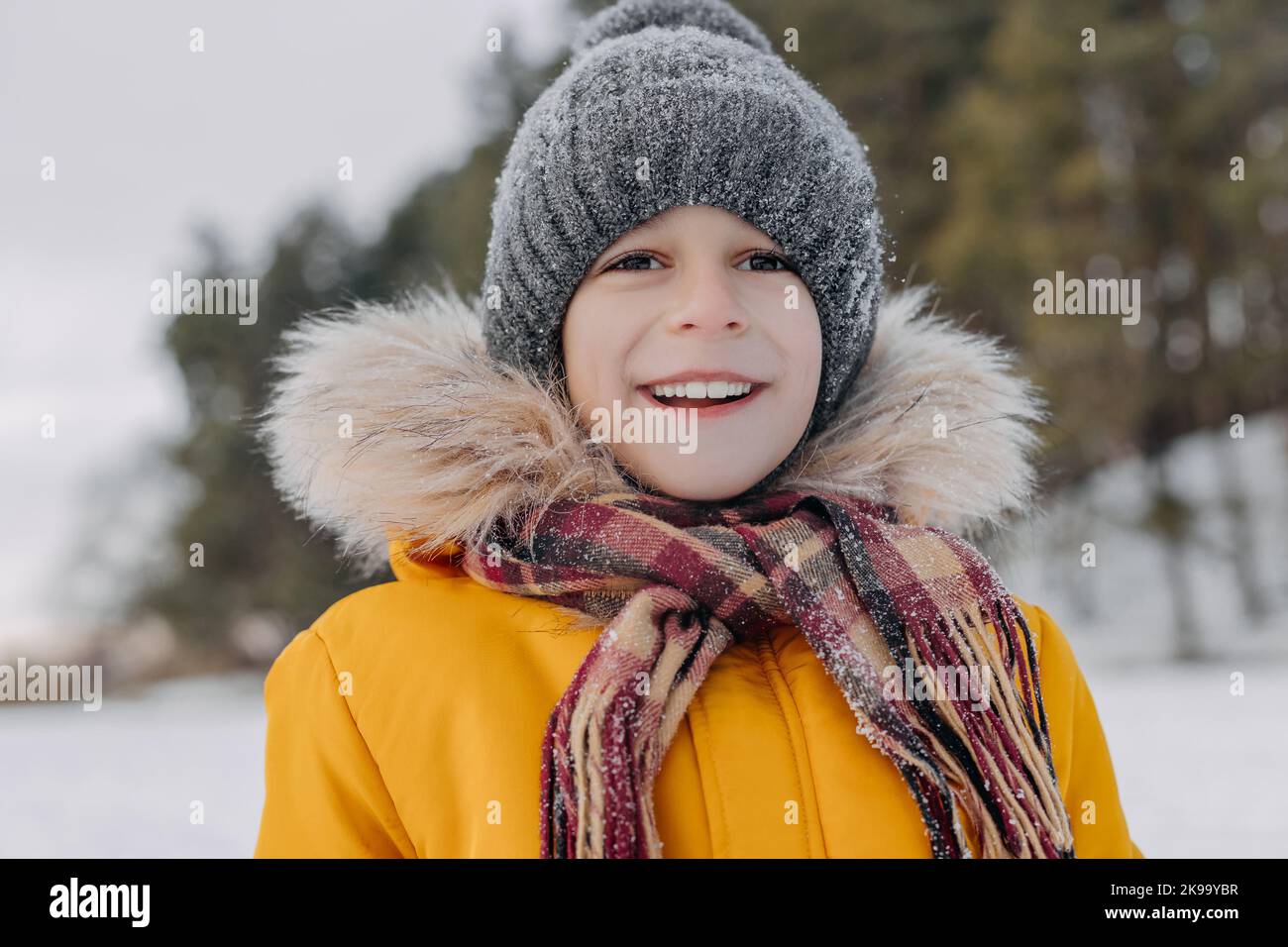 Portrait en gros plan d'un adorable enfant de 8 ans sur fond de paysage hivernal. Garçon souriant dans des vêtements chauds ayant du plaisir à l'extérieur. Concept de christma Banque D'Images