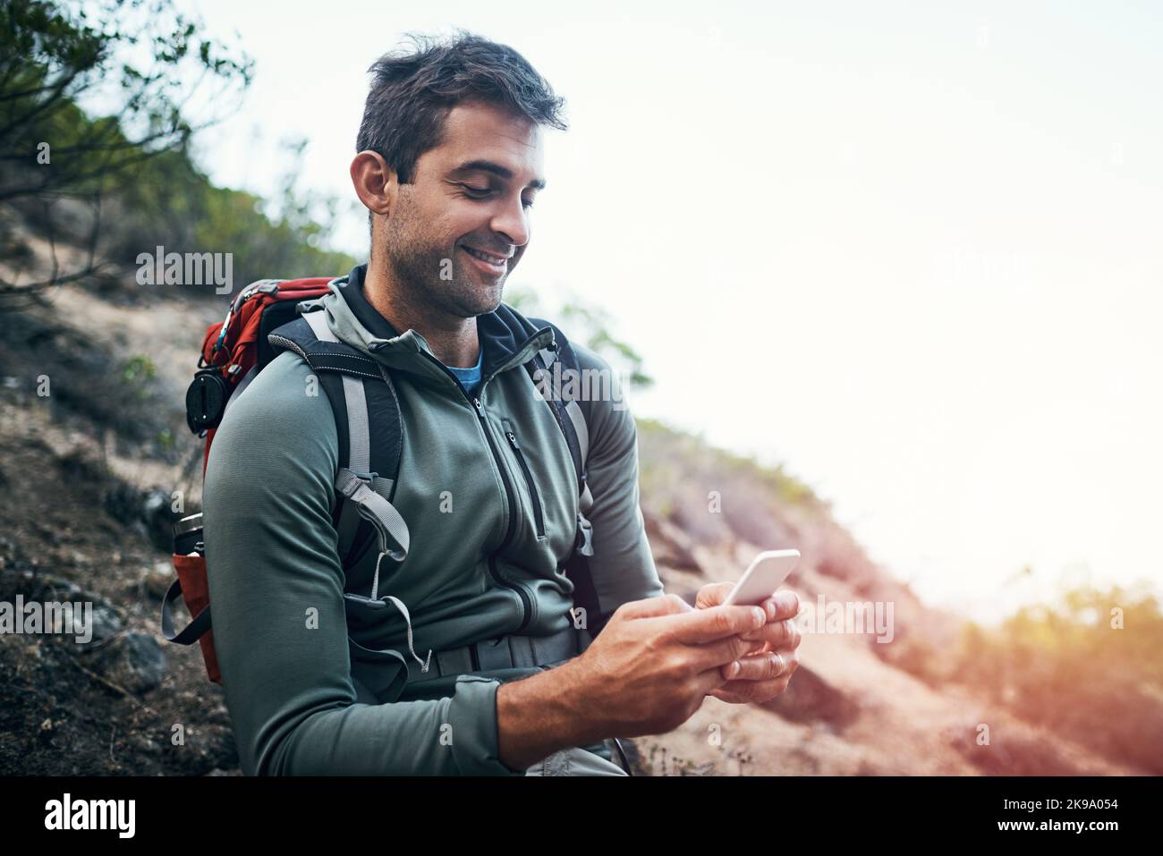 Je suis étonné que les theres signalent ici. Un jeune homme joyeux envoie des SMS sur son téléphone portable tout en allant pour une randonnée dans une montagne. Banque D'Images