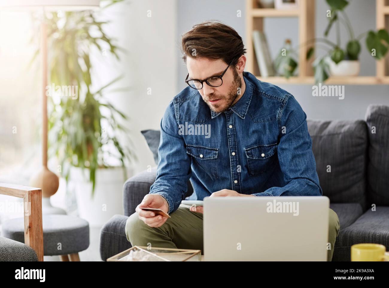 Aujourd'hui, tout le monde fait ses achats dans le confort de sa maison. Un beau jeune homme utilisant un smartphone et une carte de crédit pour faire ses achats en ligne à la maison. Banque D'Images