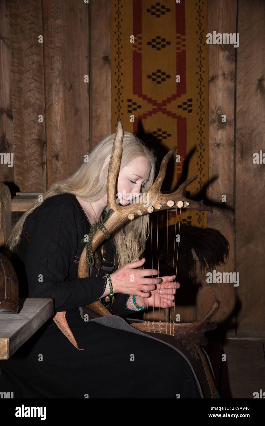 Une actrice viking jouant un instrument à cordes semblable à une harpe dans la maison de la chefferie Viking à Borg sur l'île Vestvågøya, dans l'archipel Lofoten, en Norvège. Banque D'Images