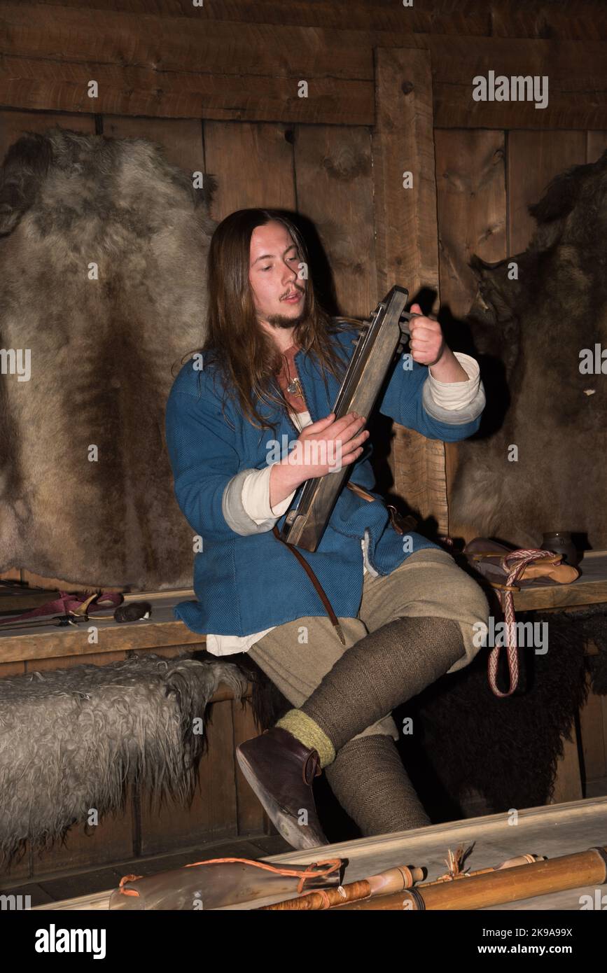 Un acteur viking jouant un instrument à cordes dans la maison d'un chef viking à Borg, sur l'île Vestvågøya, dans l'archipel des Lofoten, en Norvège. Banque D'Images