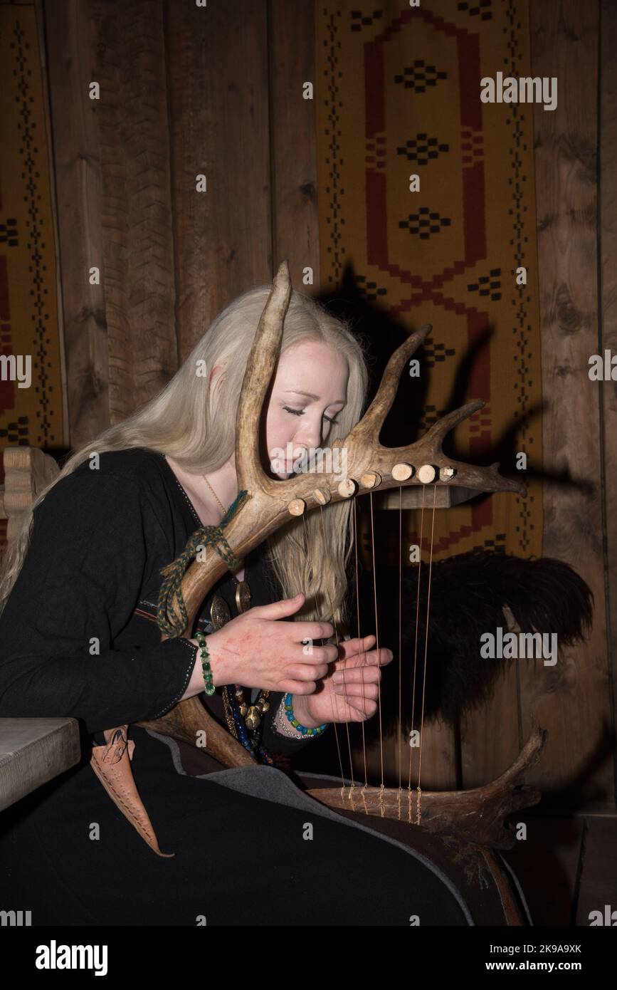 Une actrice viking jouant un instrument à cordes semblable à une harpe dans la maison de la chefferie Viking à Borg sur l'île Vestvågøya, dans l'archipel Lofoten, en Norvège. Banque D'Images