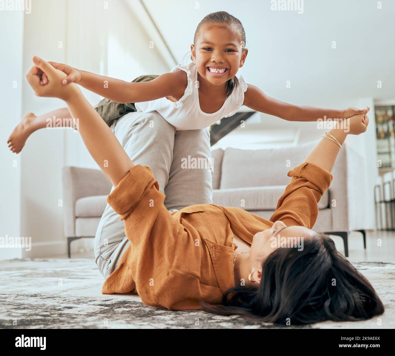 Mère ascenseur fille sur le sol et jouer dans la salle de séjour à la maison pour l'amour de famille, les soins et le bien-être. Joyeux enfant jouer amusant jeu de jeunesse avec maman et de lien dans la maison Banque D'Images