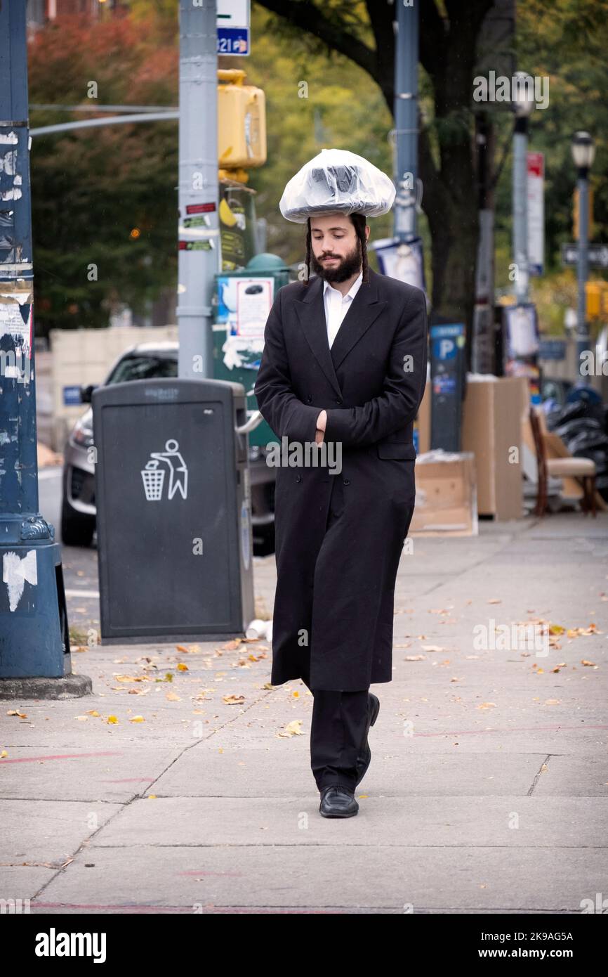 Un juif orthodoxe marchant sur l'avenue Lee pendant un bruine et portant ce qui semble être un sac protecteur de chapeau en plastique. À Brooklyn, New York, États-Unis. Banque D'Images
