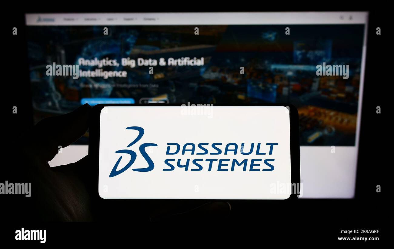 Personne tenant un smartphone avec le logo de la société de logiciels française Dassault Systemes se à l'écran devant le site Web. Mise au point sur l'affichage du téléphone. Banque D'Images