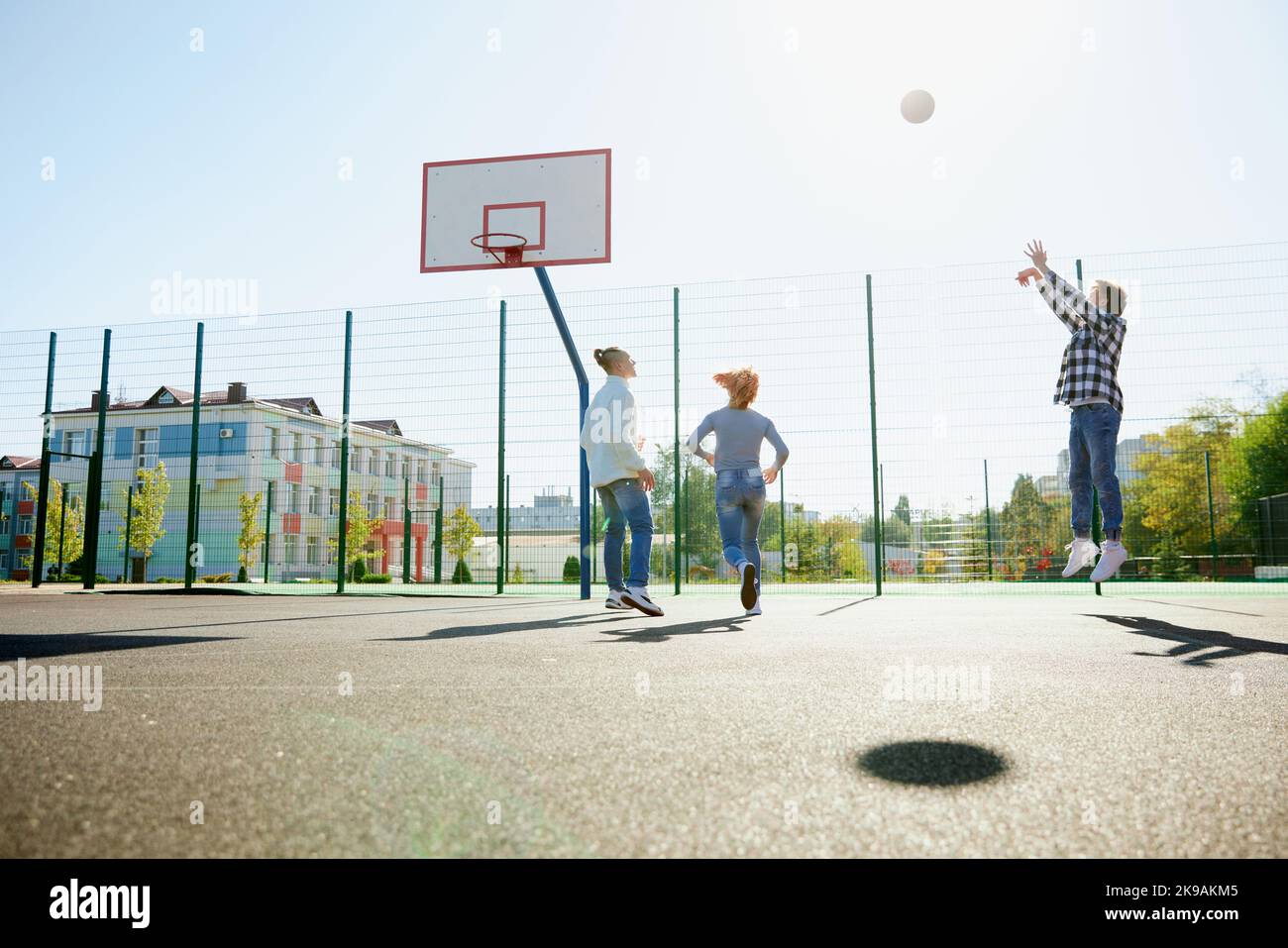 Trois adolescents jouant au streetball avec un ballon de basket-ball dans la cour de l'école après les cours. Concept de sport, activités de loisirs, passe-temps, équipe, amitié Banque D'Images