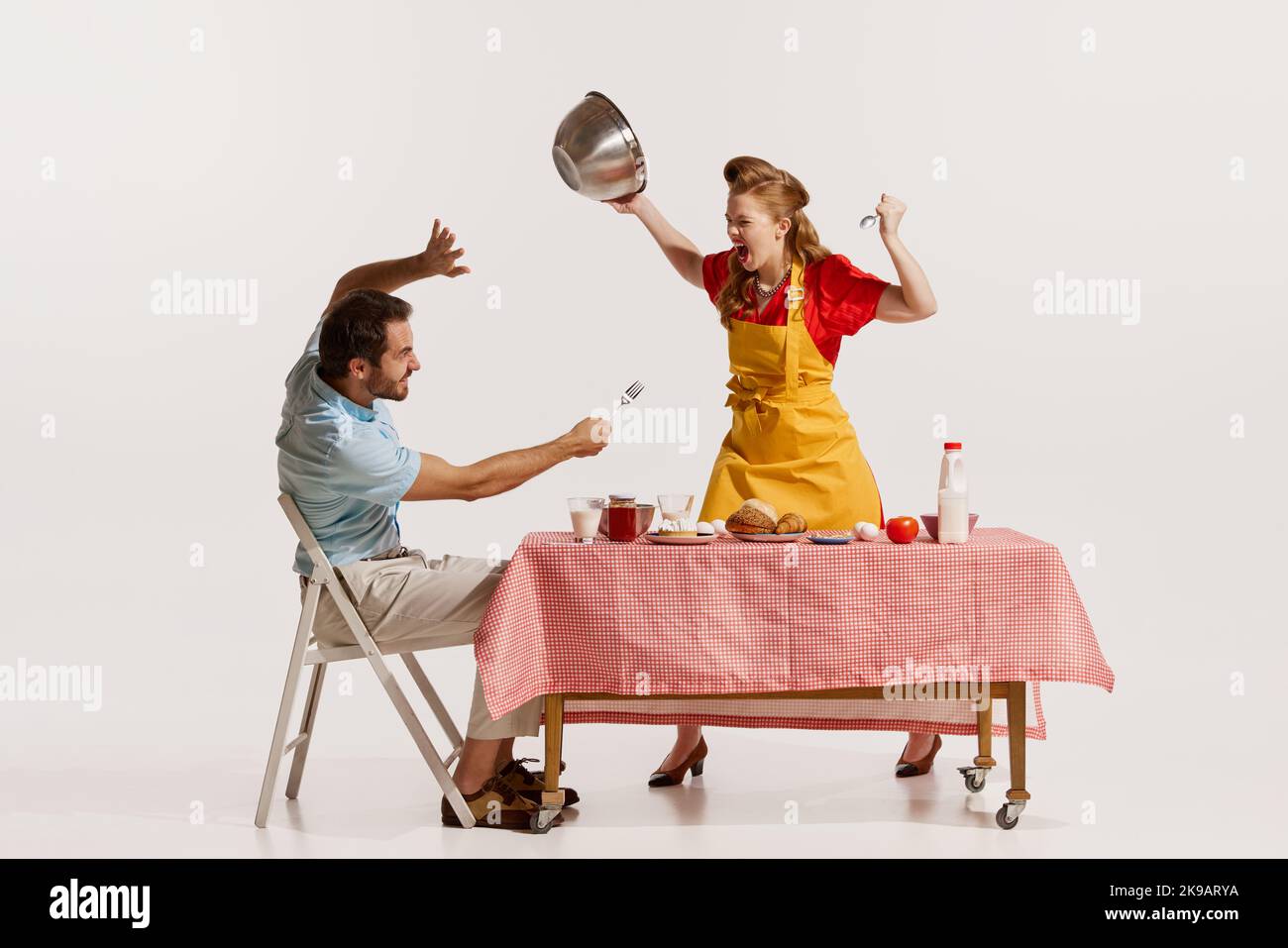 Portrait d'un jeune couple émotif fort, en train de se quereller agressivement tout en prenant le petit déjeuner isolé sur fond blanc. Banque D'Images