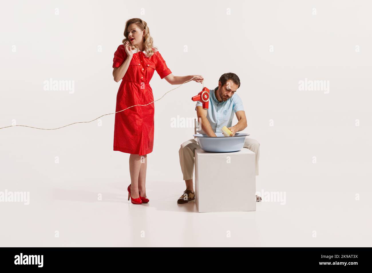 Portrait de l'homme lavant la vaisselle pendant que la femme parle au téléphone et tenant le sèche-cheveux sur l'eau isolée sur fond blanc Banque D'Images
