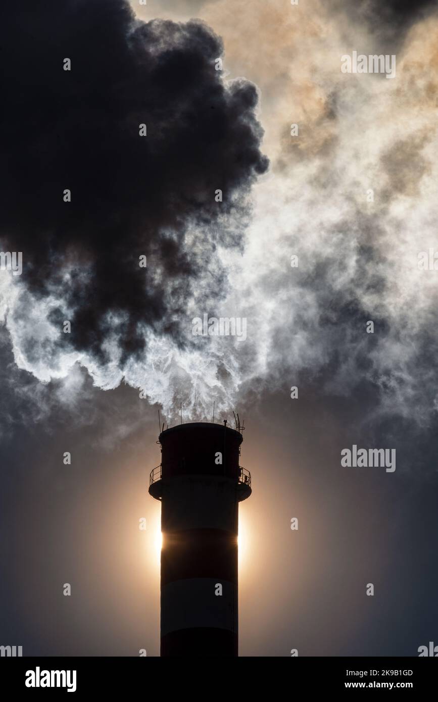 Fumée sombre et vapeur de cheminée en usine contre le soleil sur le ciel Banque D'Images