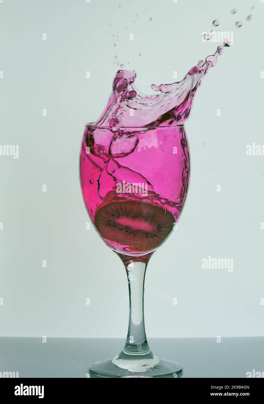 Fruits éclaboussant dans le vin, l'esprit, le verre à cocktail, magnifique cadre de gel de gouttelettes d'eau liquide rose vibrantes dispersées dans l'air pour les bars, la fête, les pubs. Banque D'Images