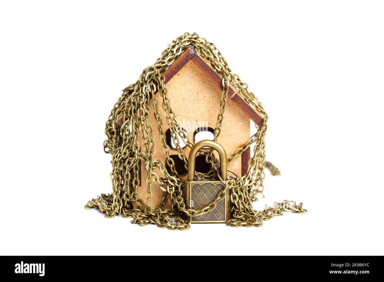 Maison de jouets en bois enveloppée dans des chaînes avec un cadenas de couleur bronze isolé sur blanc. Banque D'Images