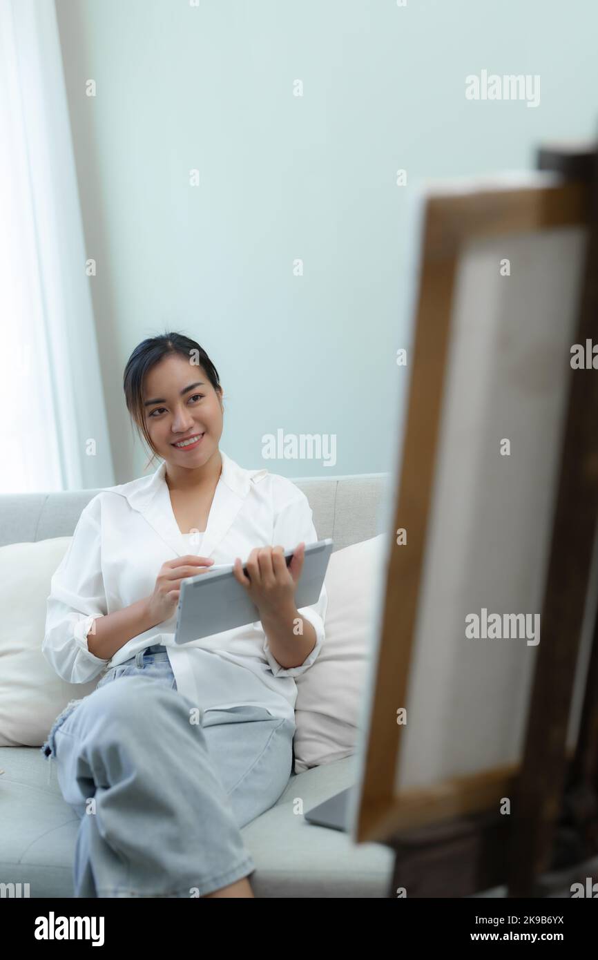 Portrait d'une femme asiatique utilisant une tablette pour peindre des œuvres d'art sur un canapé. Banque D'Images
