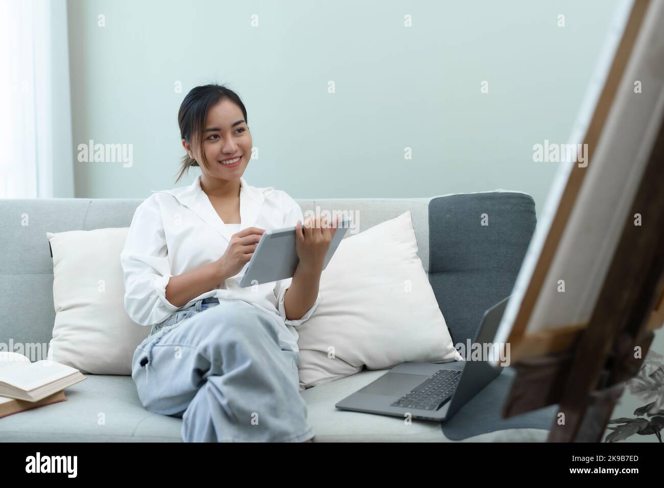 Portrait d'une femme asiatique utilisant une tablette pour peindre des œuvres d'art sur un canapé. Banque D'Images