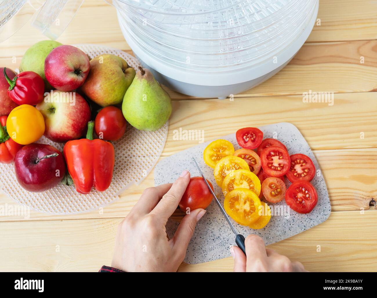 Sèche-linge électrique pour déshydrater des produits avec chargement horizontal de palettes. Vue de dessus, une fille coupe des tomates pour sécher, gros plan, lumière naturelle Banque D'Images