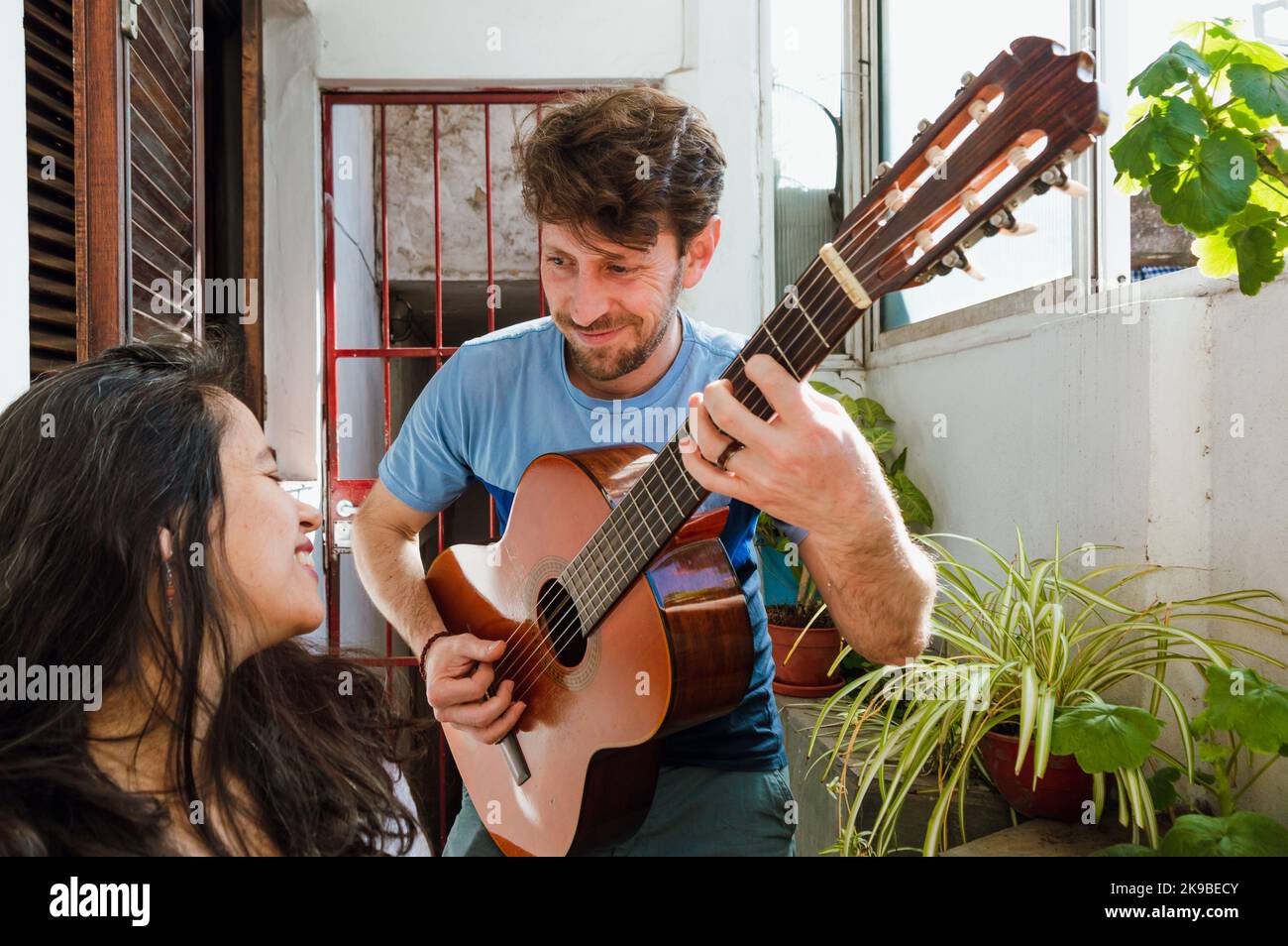 jeune homme du caucase du sud avec une barbe, à la maison souriant serenade avec sa guitare et chante des chansons à sa femme enceinte qui est heureuse du voir. Banque D'Images