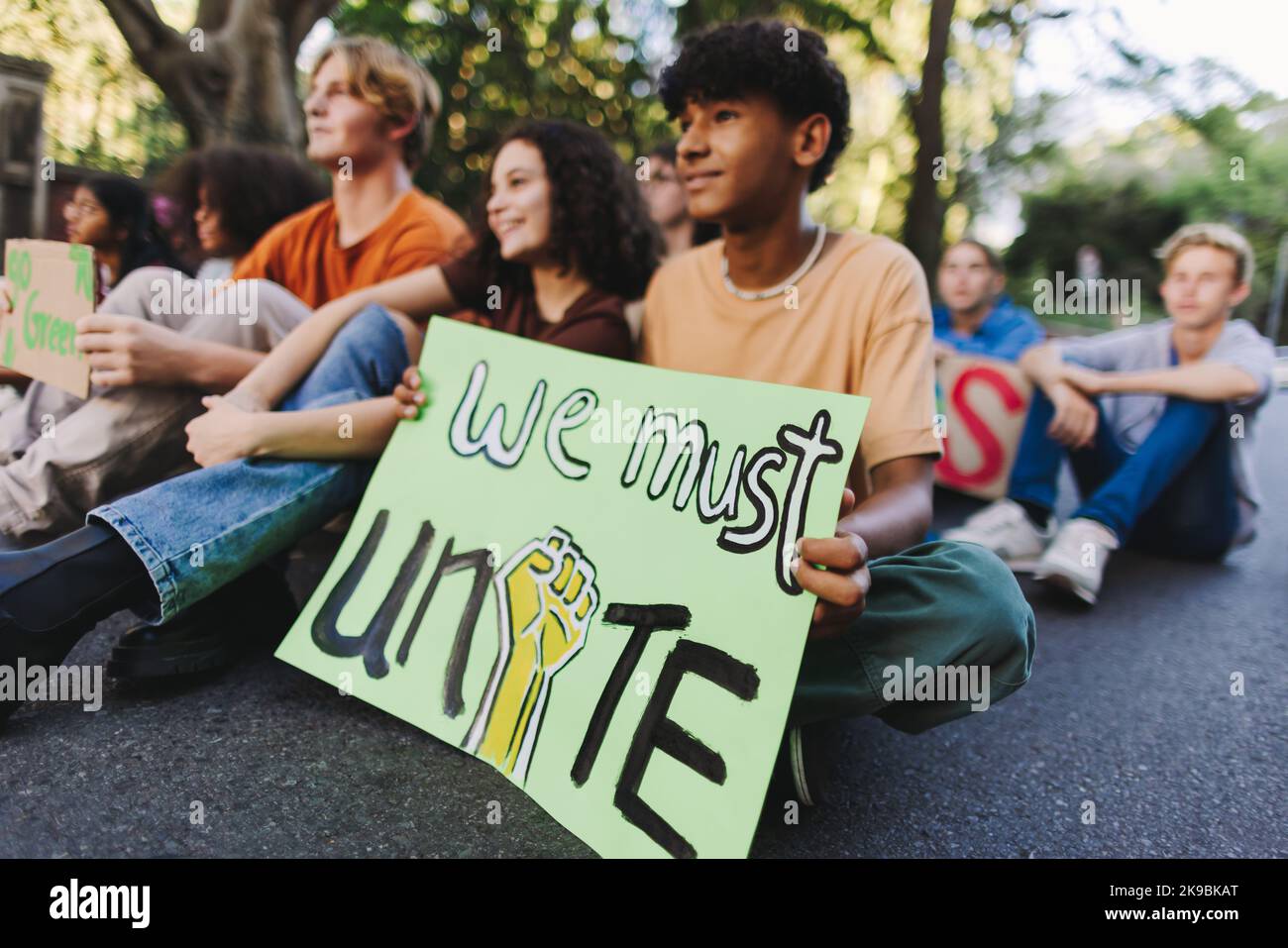 Un adolescent tenant une affiche alors qu'il était assis avec un groupe de jeunes manifestants lors d'une manifestation contre le changement climatique. Jeunes multiculturels rejoignant le Glo Banque D'Images
