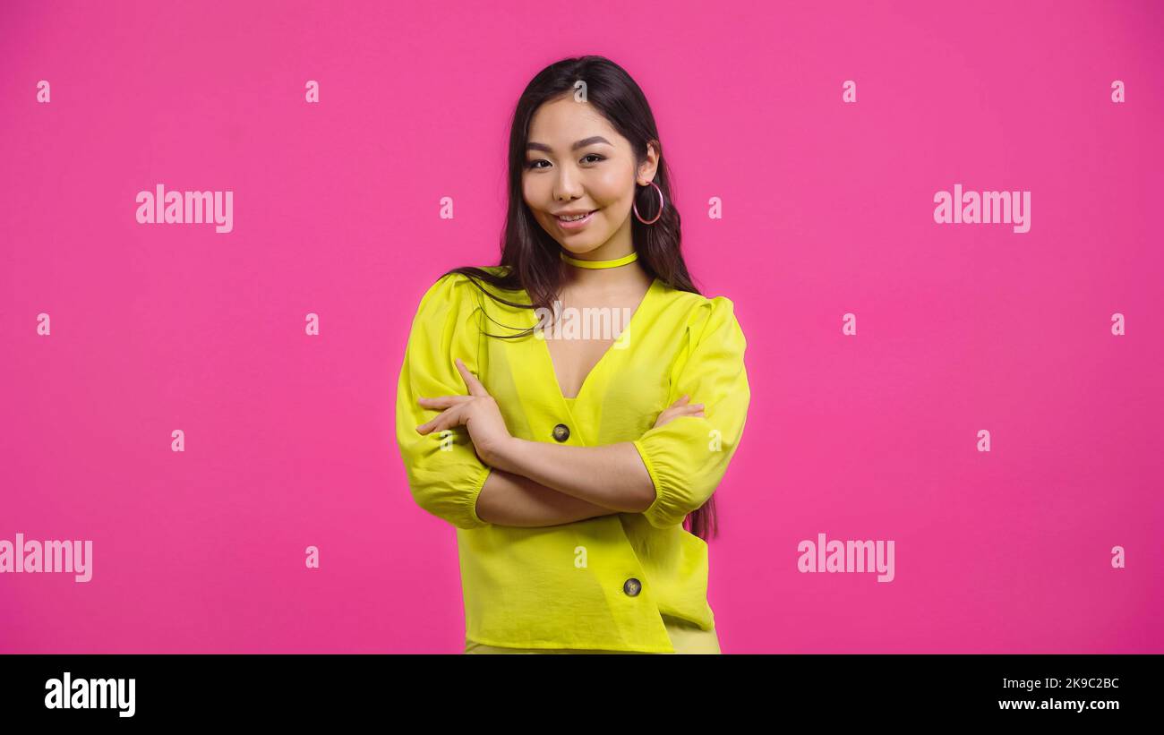 jolie femme asiatique debout avec des bras croisés isolée sur rose Banque D'Images