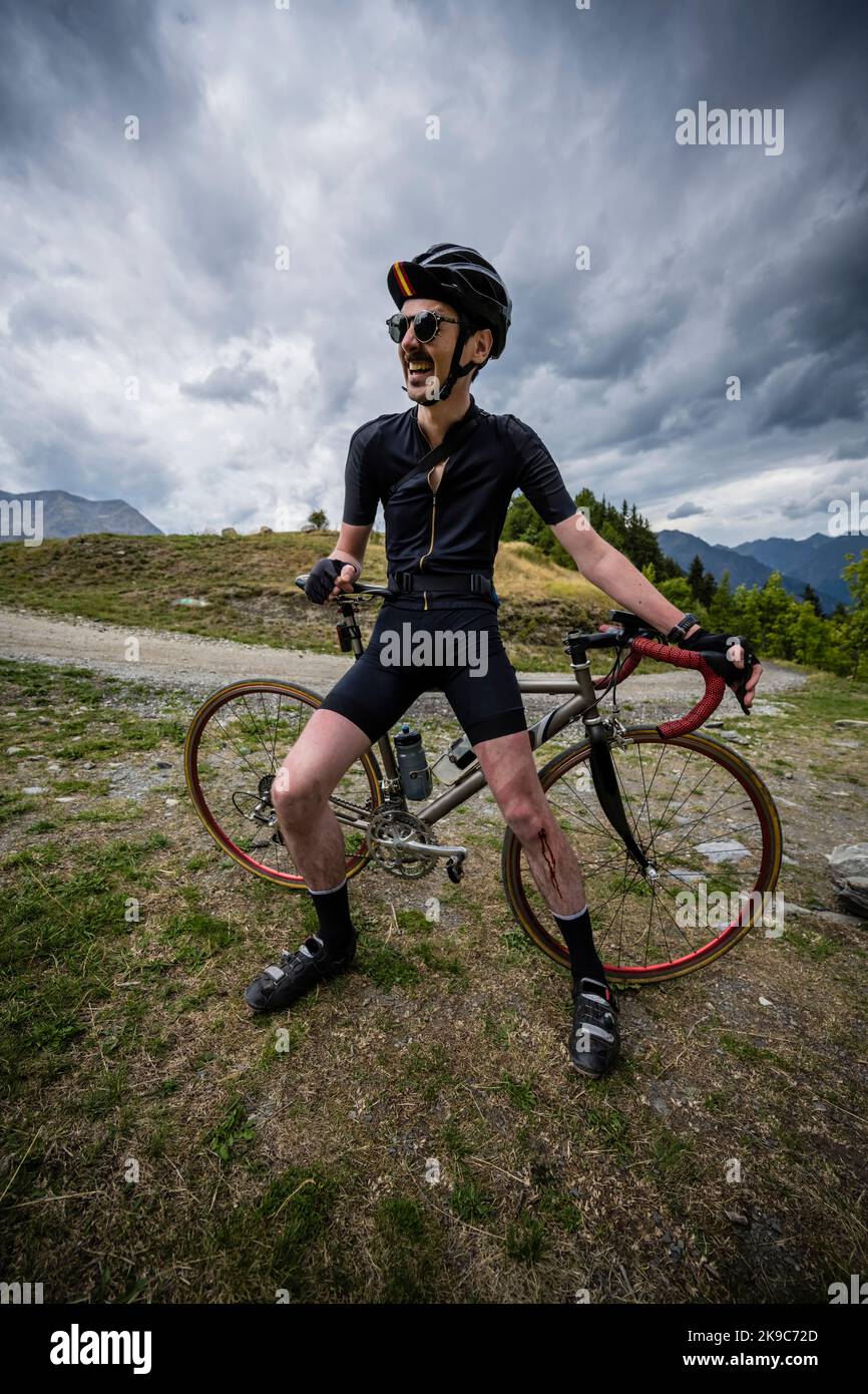 Cycliste masculin prenant un repos du vélo de gravier et évaluant sa jambe blessée, Villard Raymond village de montagne, Alpes françaises. Banque D'Images
