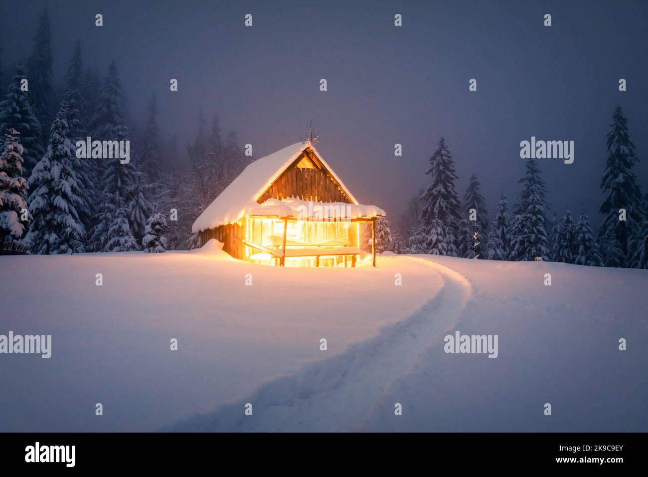 Paysage d'hiver fantastique avec cabine en bois lumineux dans une forêt enneigée. Maison confortable dans les montagnes de Carpathian. Concept de vacances de Noël Banque D'Images