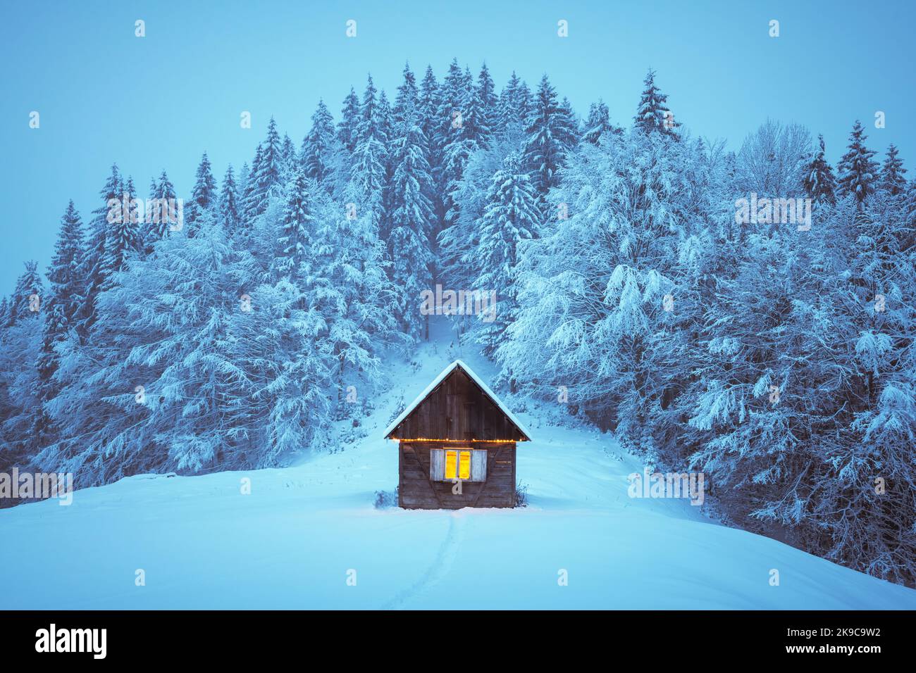 Paysage d'hiver fantastique avec cabine en bois lumineux dans une forêt enneigée. Maison confortable dans les montagnes de Carpathian. Concept de vacances de Noël Banque D'Images