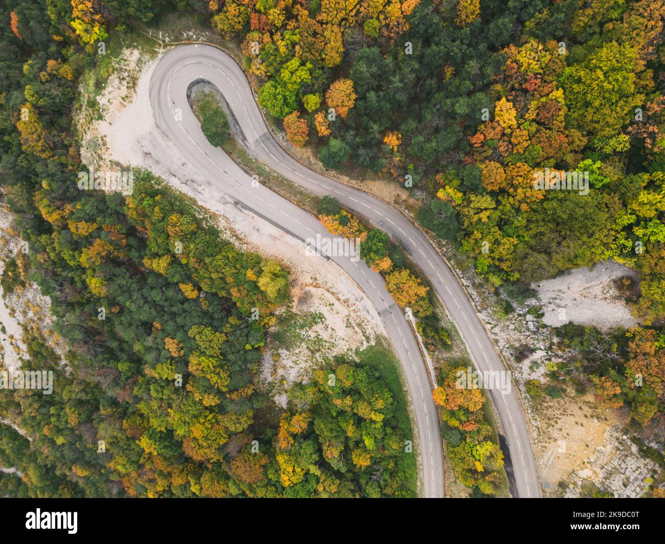 Vue aérienne d'une route sinueuse depuis un col de haute montagne à travers une forêt d'automne dense et colorée. Banque D'Images