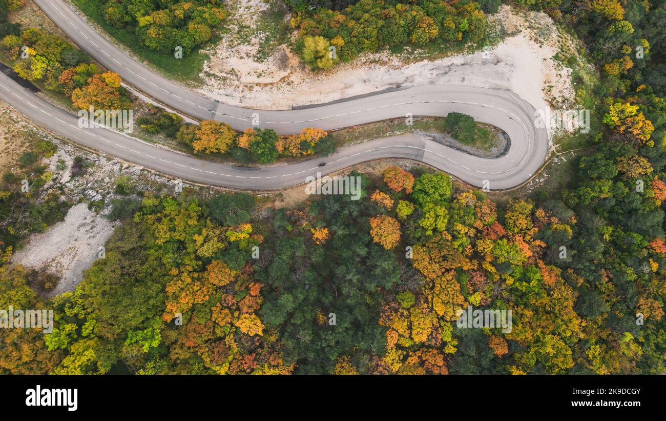 Vue aérienne d'une route sinueuse depuis un col de haute montagne à travers une forêt d'automne dense et colorée. Banque D'Images