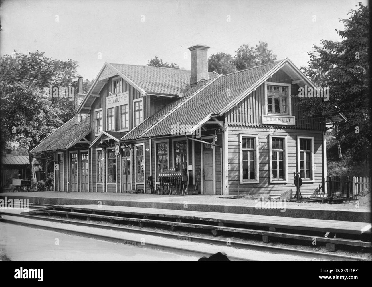 Gare de Lammhult. Marron clair avec noeuds jaunes mats, moulures et doublure, portes vertes et arches de fenêtres. Le toit ardoise rouge brun. Les signes jaune mat comme les moulures de style brun. Clôture t droite rouge m allée blanche. Cheminée en briques rouges. Banque D'Images