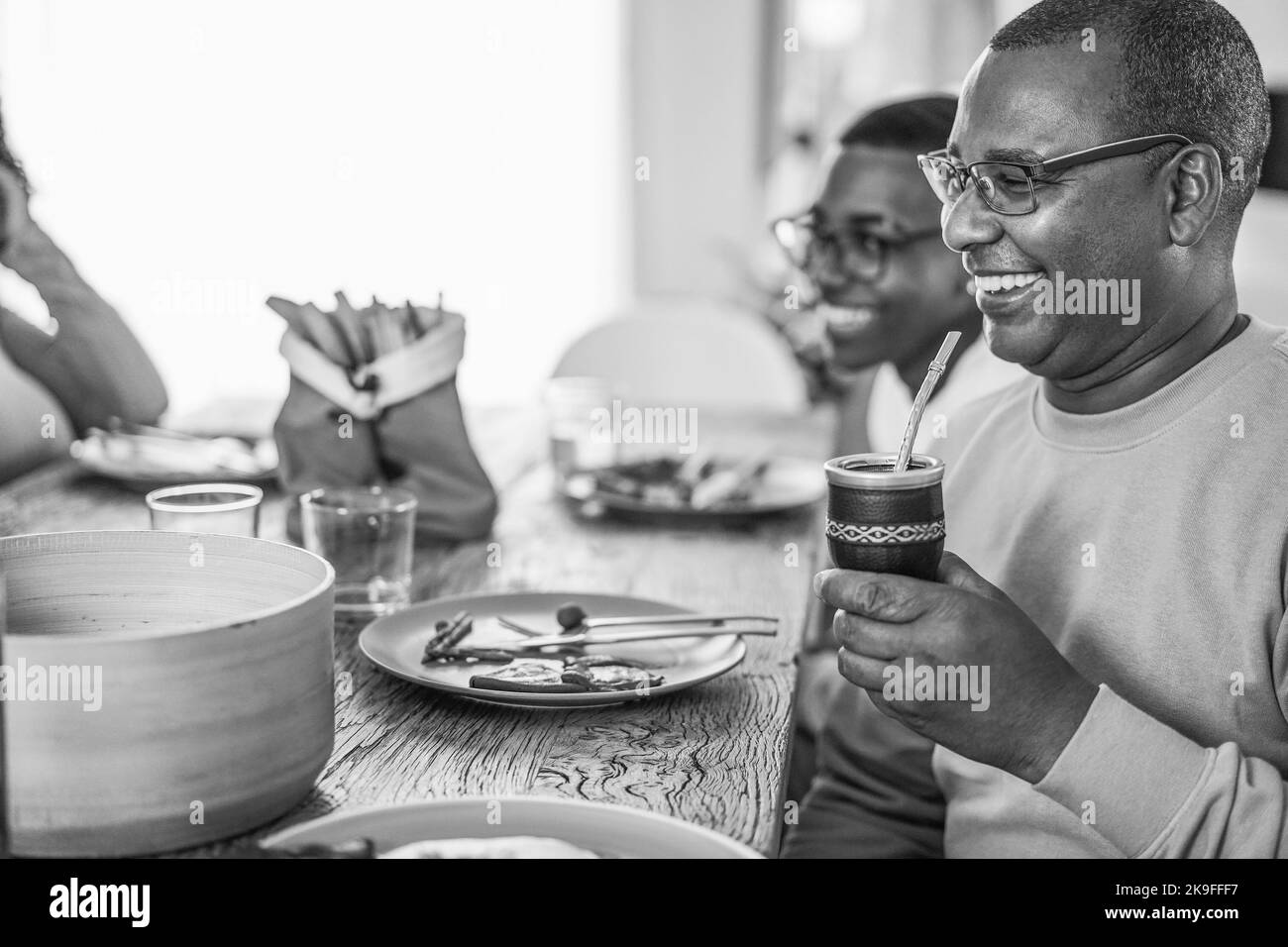 Heureux père noir buvant yerba mate pendant le déjeuner à la maison - foyer principal sur la paille - montage noir et blanc Banque D'Images