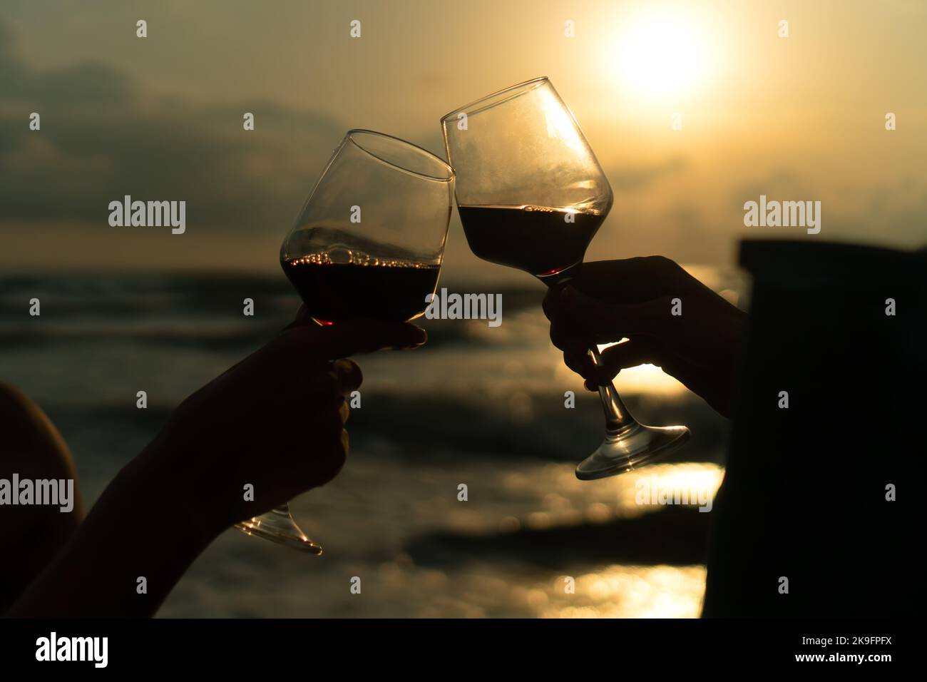 Silhouette rapprochée de deux verres de vin se clinquant sur le fond de la mer au coucher du soleil. Concept de célébration, romance, amitié Banque D'Images
