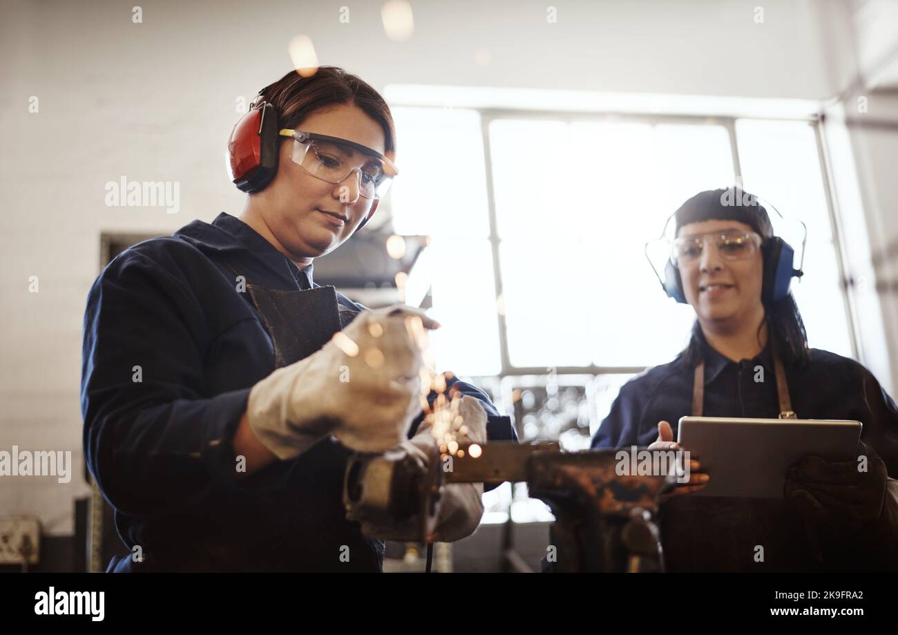 Thats parfait. Deux jeunes artisans attirants utilisant une meuleuse d'angle dans leur atelier. Banque D'Images