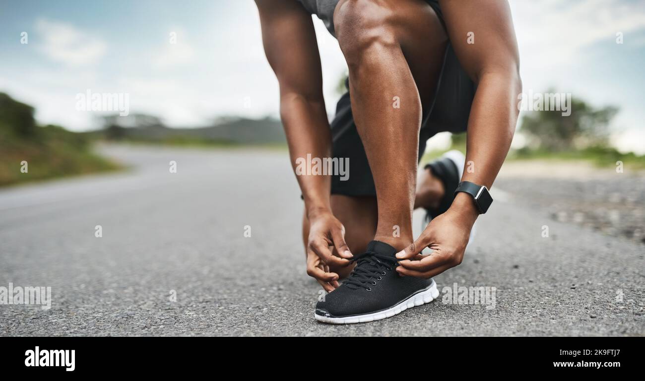 Passez au-delà de tout obstacle. Gros plan d'un sportif qui noue ses lacets tout en faisant de l'exercice à l'extérieur. Banque D'Images