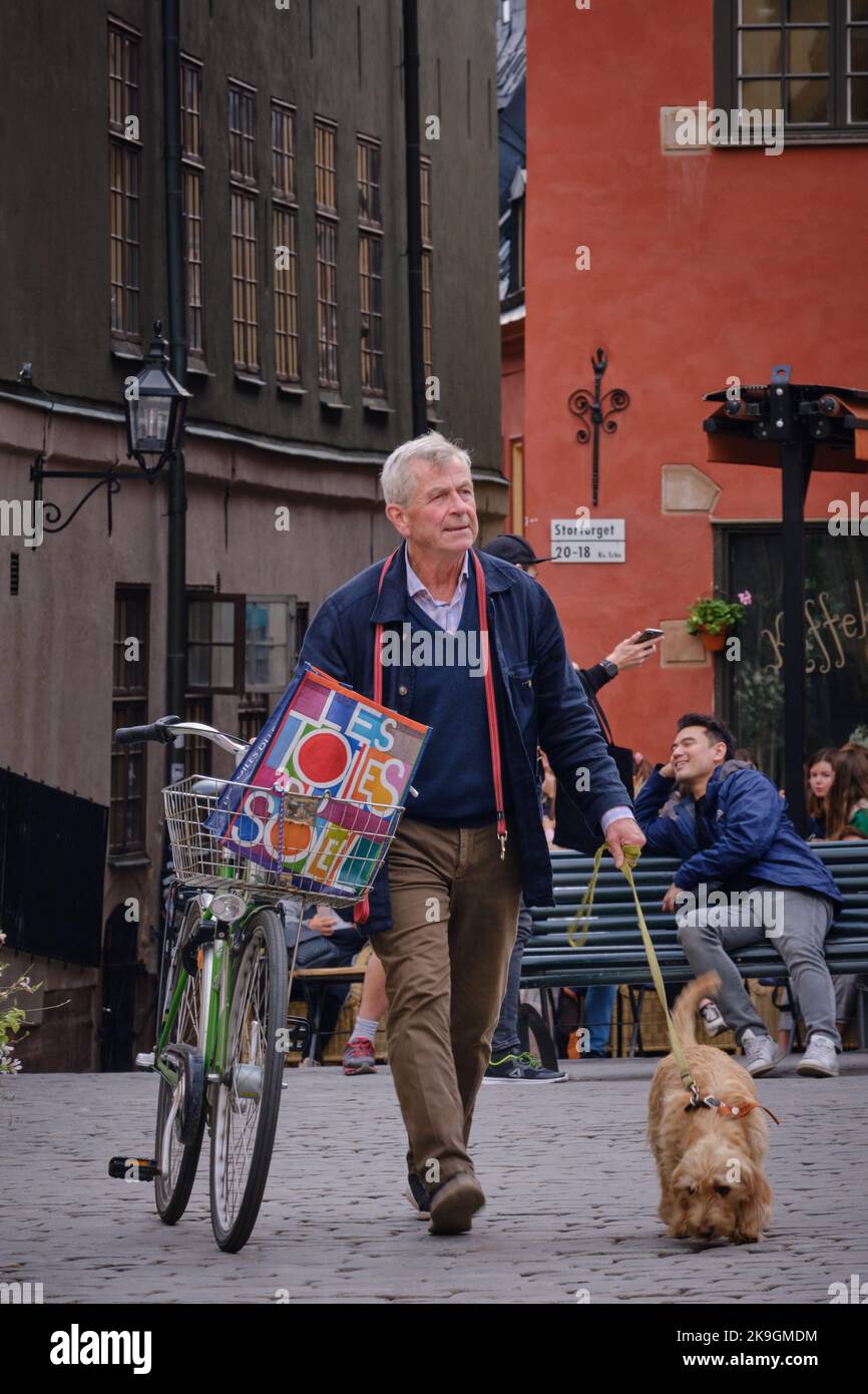 Stockholm, Suède - 2022 septembre : un vieil homme marchant avec un vélo et un chien devant les bâtiments emblématiques rouges et jaunes de Stortorget, à Gamla Stan Banque D'Images
