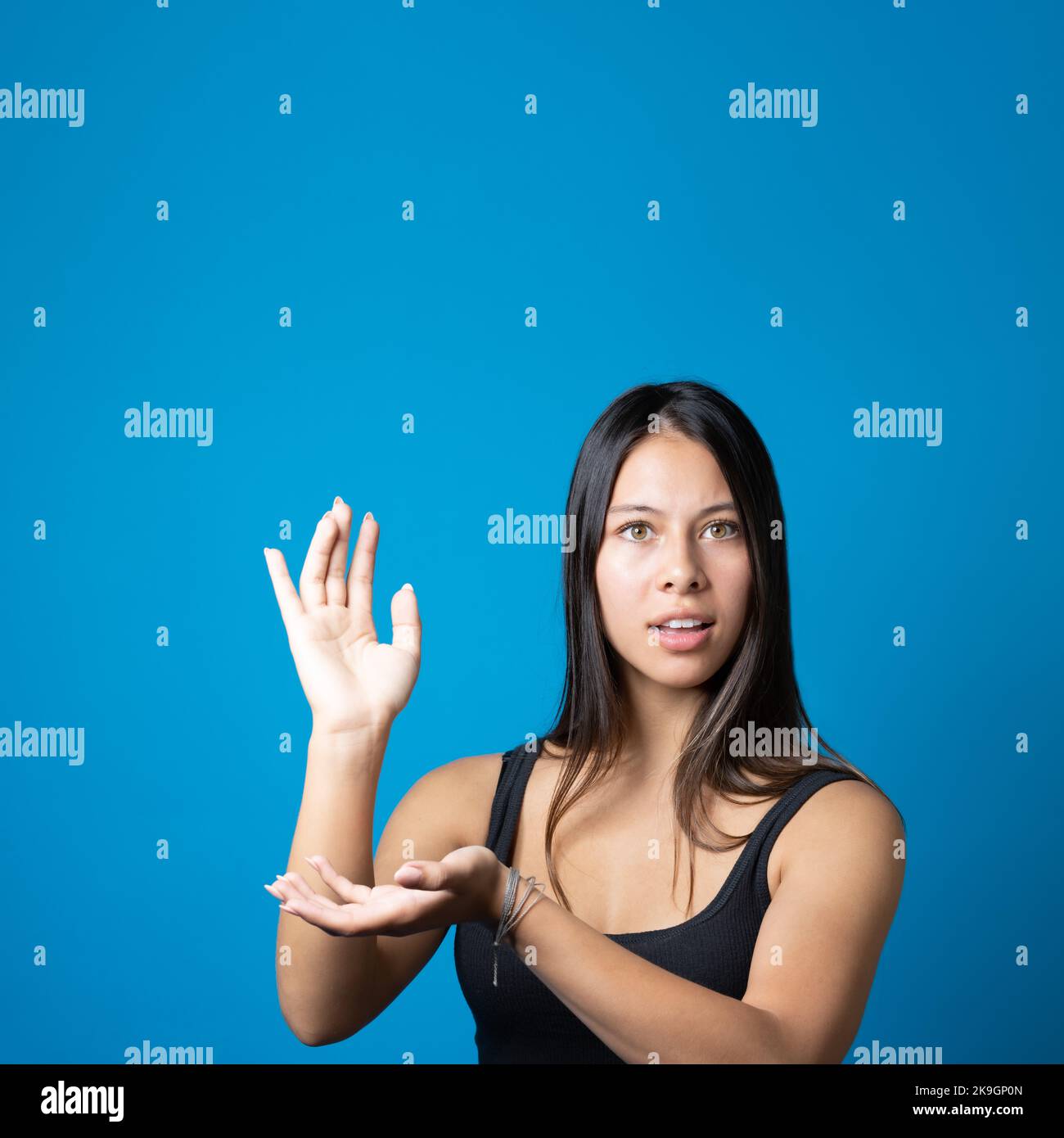 Jeune femme branchée et confuse regardant l'appareil photo et tenant et présentant l'espace de copie sur sa paume isolée sur fond bleu Banque D'Images