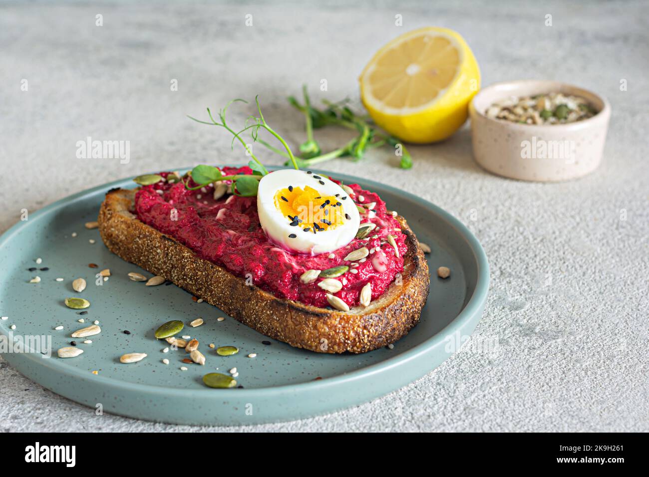 Toast au grain entier avec houmous de betterave, graines, œufs et microverts (pousses de pois germées) sur fond gris clair. Le concept de saine alimentation. Banque D'Images