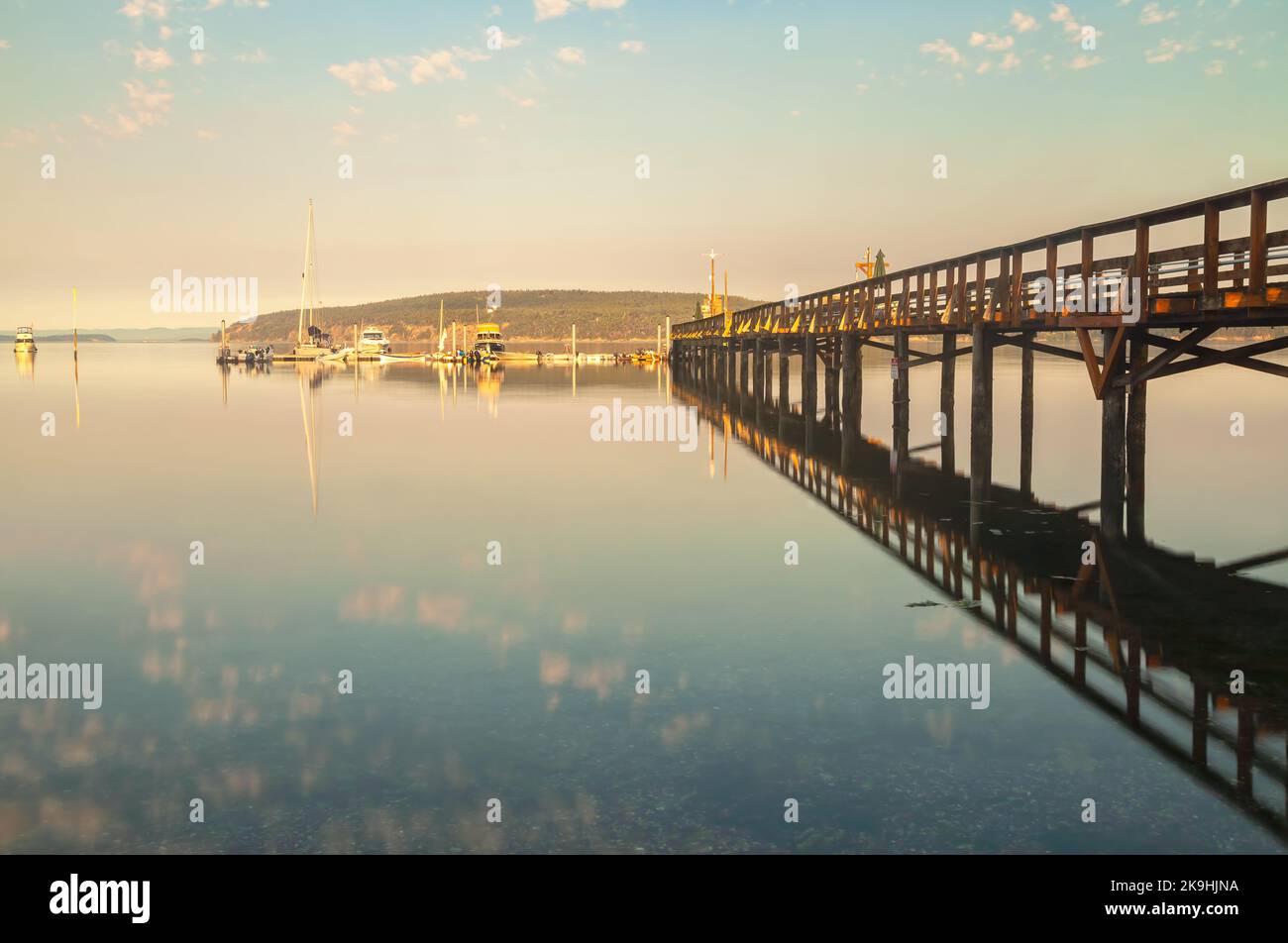 Une longue jetée en bois s'étend sur l'eau calme et calme du port d'Orcas Island, Washington, son reflet parfaitement reflété dans la surface. Banque D'Images