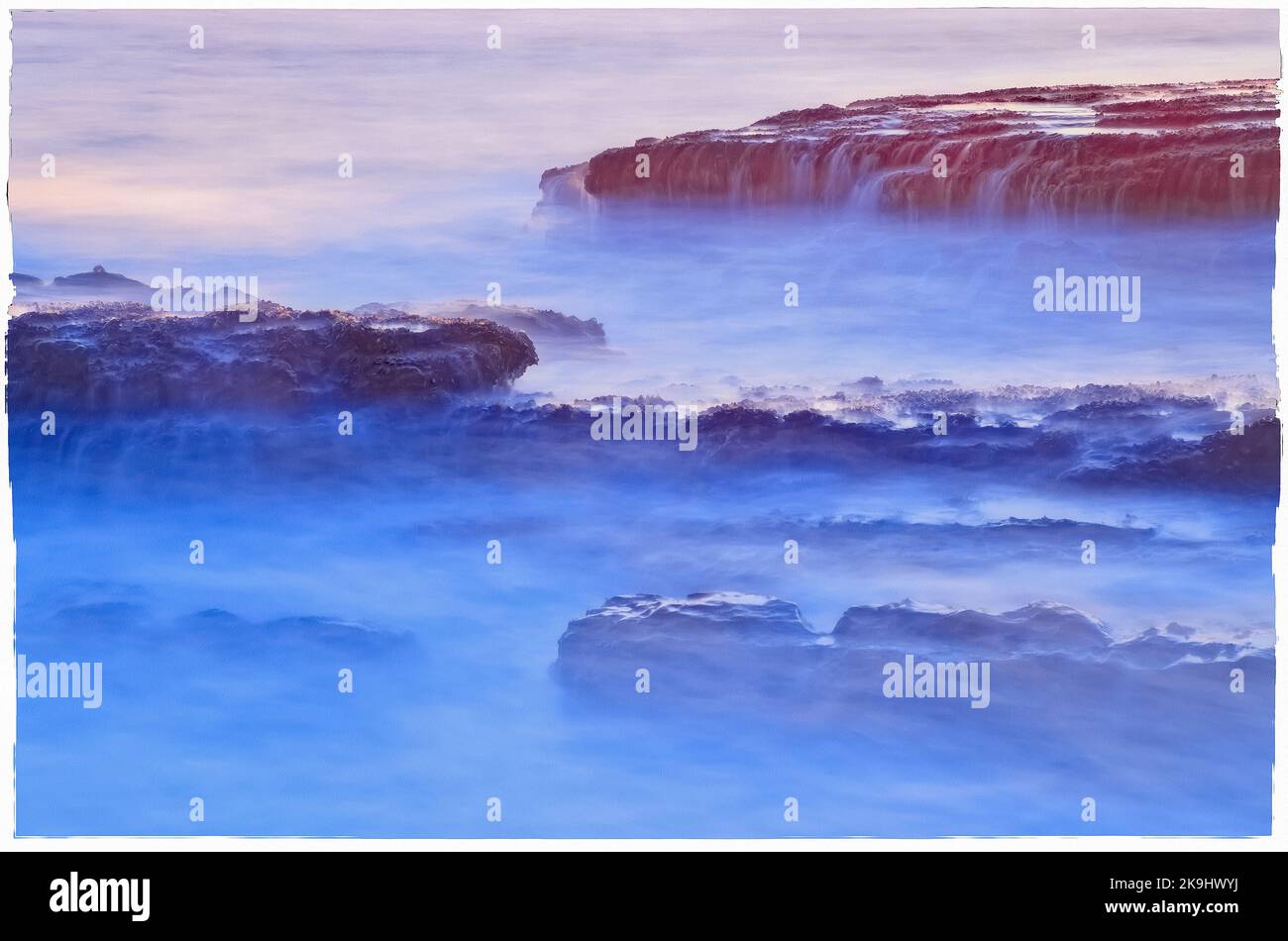 L'image capture un paysage marin serein avec un accent sur des formations rocheuses partiellement immergées dans l'eau. Banque D'Images