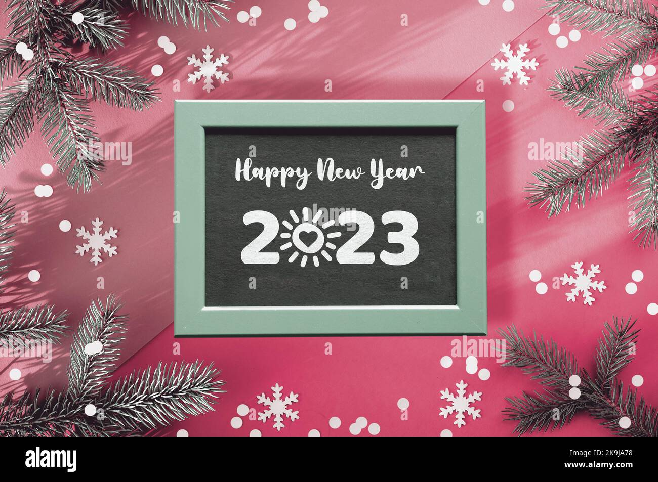 Bonne année 2023, soleil avec coeur dessin animé à la place de zéro chiffre. Arrière-plan d'hiver simple. Branches de sapin sur papier rose bicolore avec confetti Banque D'Images