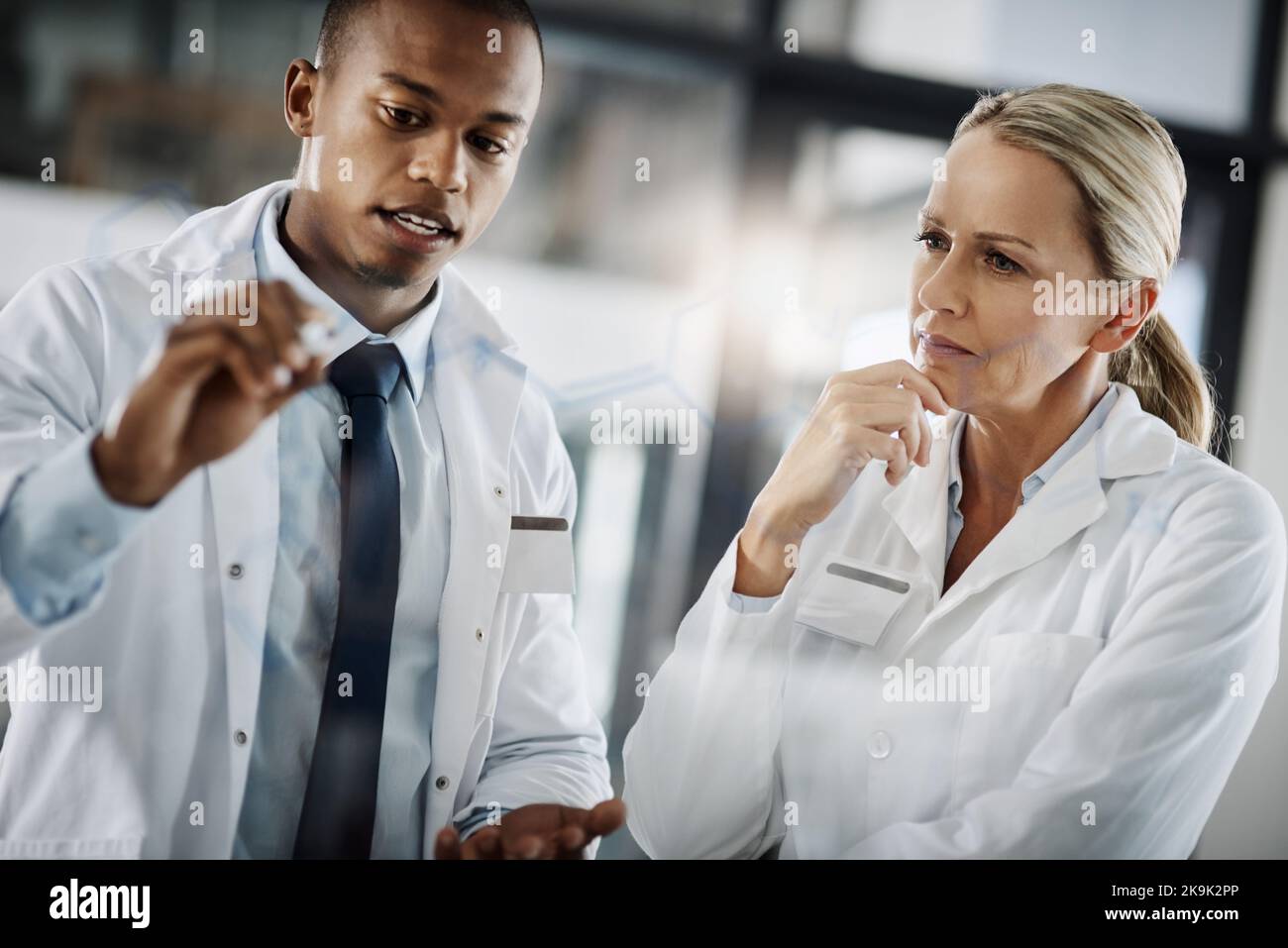 Deux scientifiques rédigeant des formules sur un plateau de verre tout en effectuant des recherches dans leur laboratoire. Banque D'Images