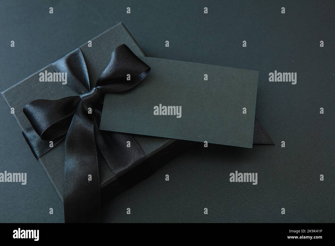 Soldes du Vendredi fou et cadeaux de Noël. Boîte cadeau avec ruban noir et carte vide isolée sur fond noir, Banque D'Images