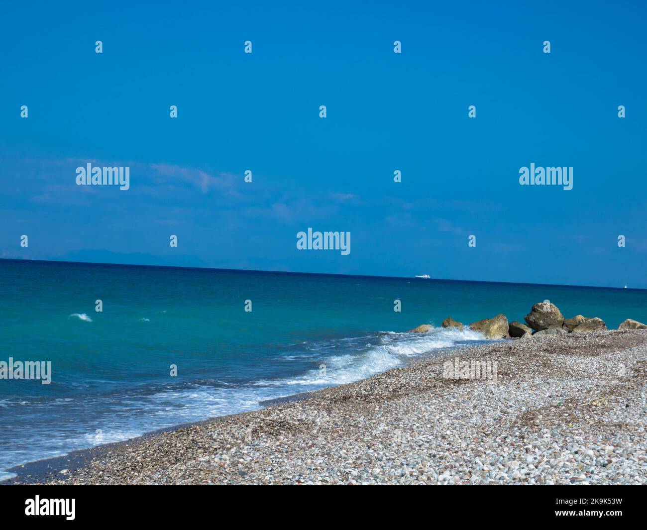 Belle plage déserte sur la côte ouest de Rhodes près de Kamiros. Eau de mer turquoise, ciel bleu sans nuages, plage de galets. Banque D'Images