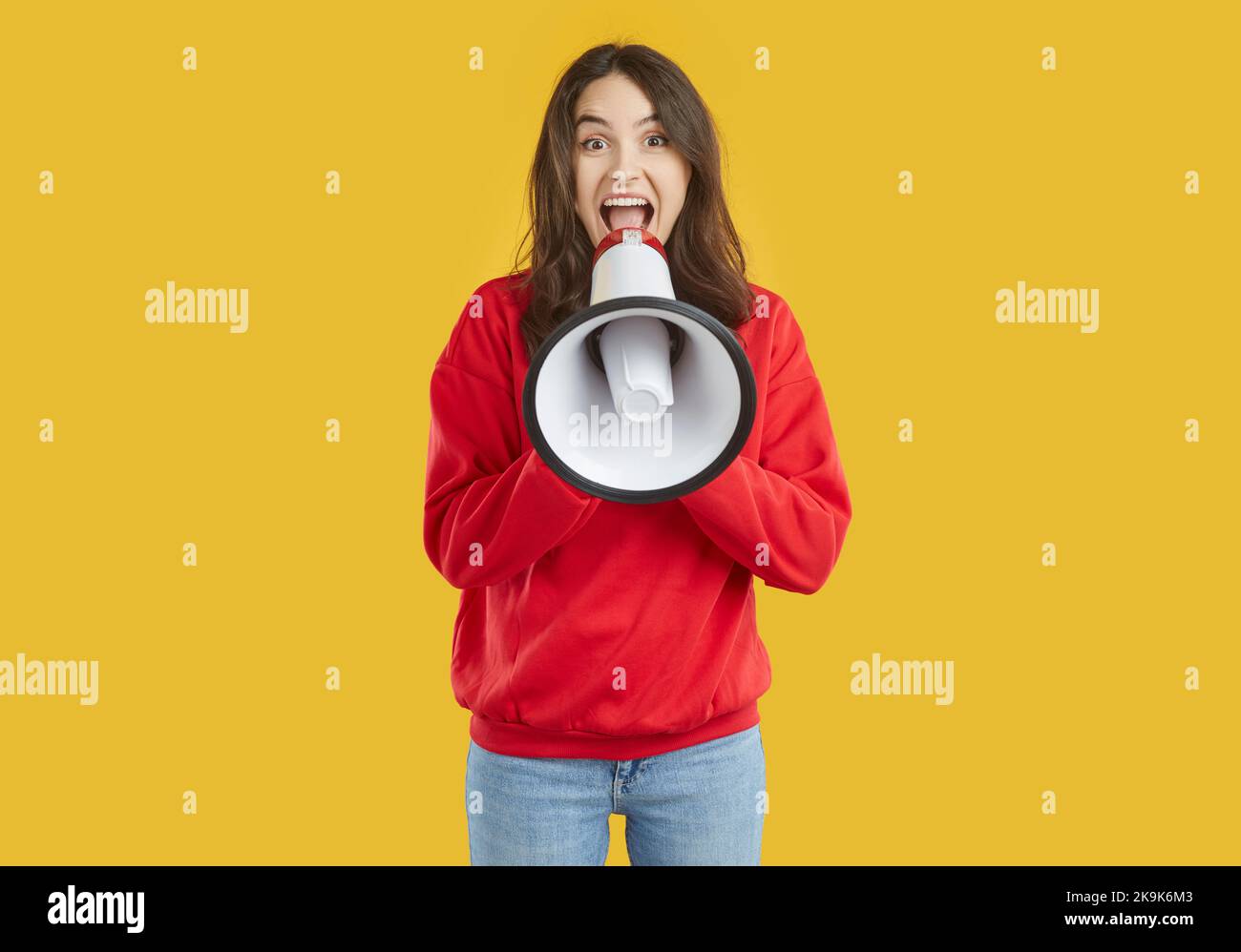 Une jeune femme brune portant un sweat-shirt rouge rit en parlant dans un haut-parleur sur fond jaune. Banque D'Images