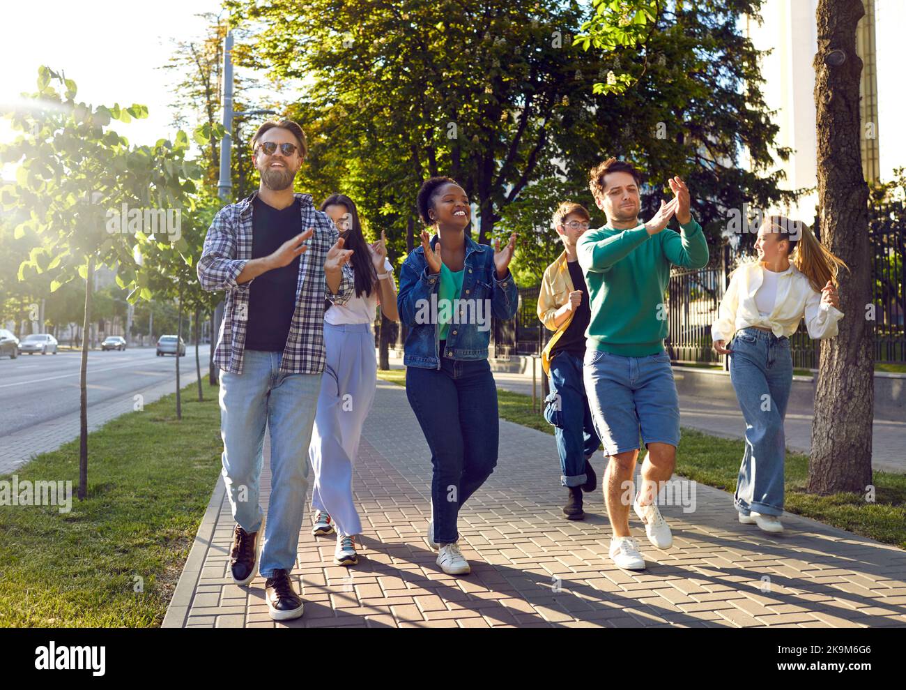 Des amis énergiques et gaies se promissent dans les rues de la ville en soirée d'été et s'amusent à danser. Banque D'Images