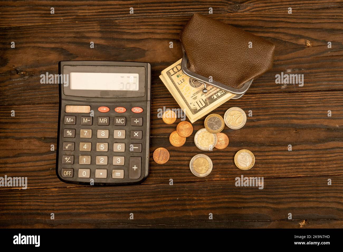 Billets en dollars, pièces en euros, portefeuille en cuir brun vintage et calculatrice sur une surface en bois. Gros plan, mise au point sélective. Banque D'Images