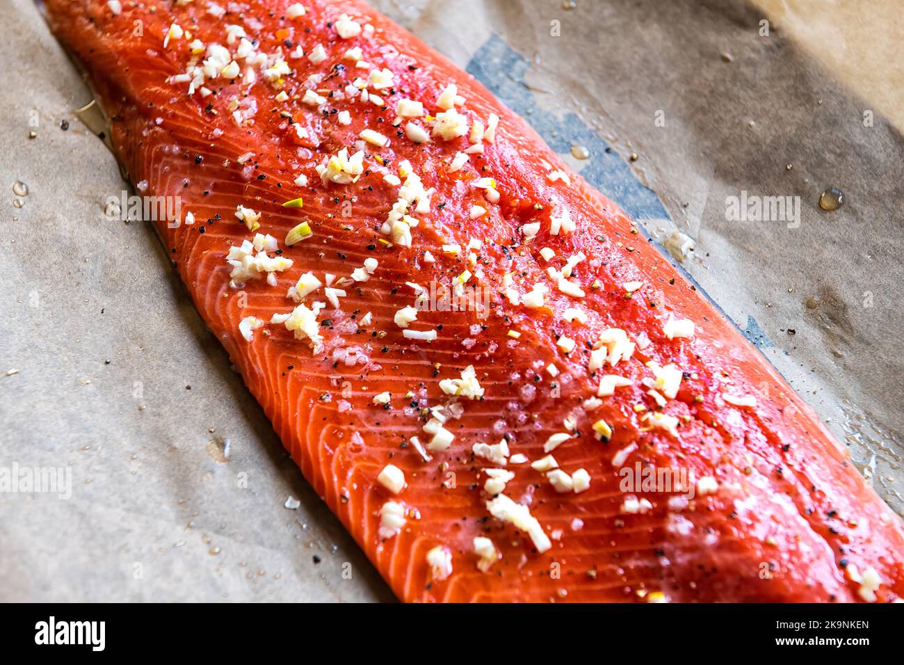 Macro-gros plan du saumon sockeye cru non cuit préalablement congelé avec sel, poivre et assaisonnement à l'ail sur papier sulfurisé de la plaque du four Banque D'Images