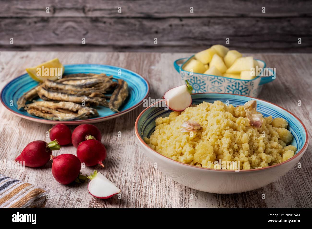 Assiette de migas, cuisine espagnole traditionnelle, accompagnée de radis, de poisson et de melon sur une table en bois. Banque D'Images