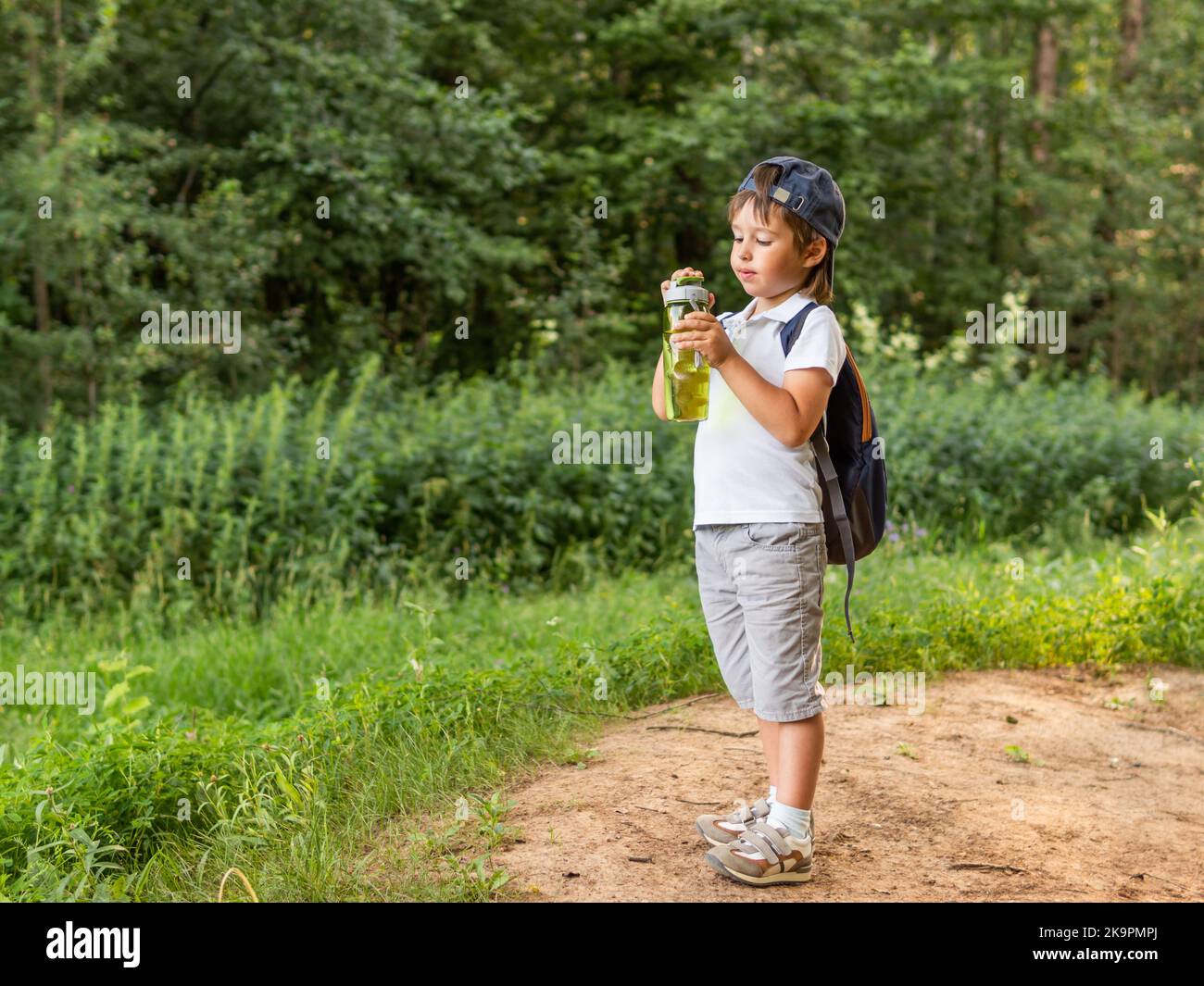 Un garçon assoiffé tient dans les mains un flacon vert réutilisable avec de l'eau pure. Activités de plein air en été. Un mode de vie sain. Banque D'Images