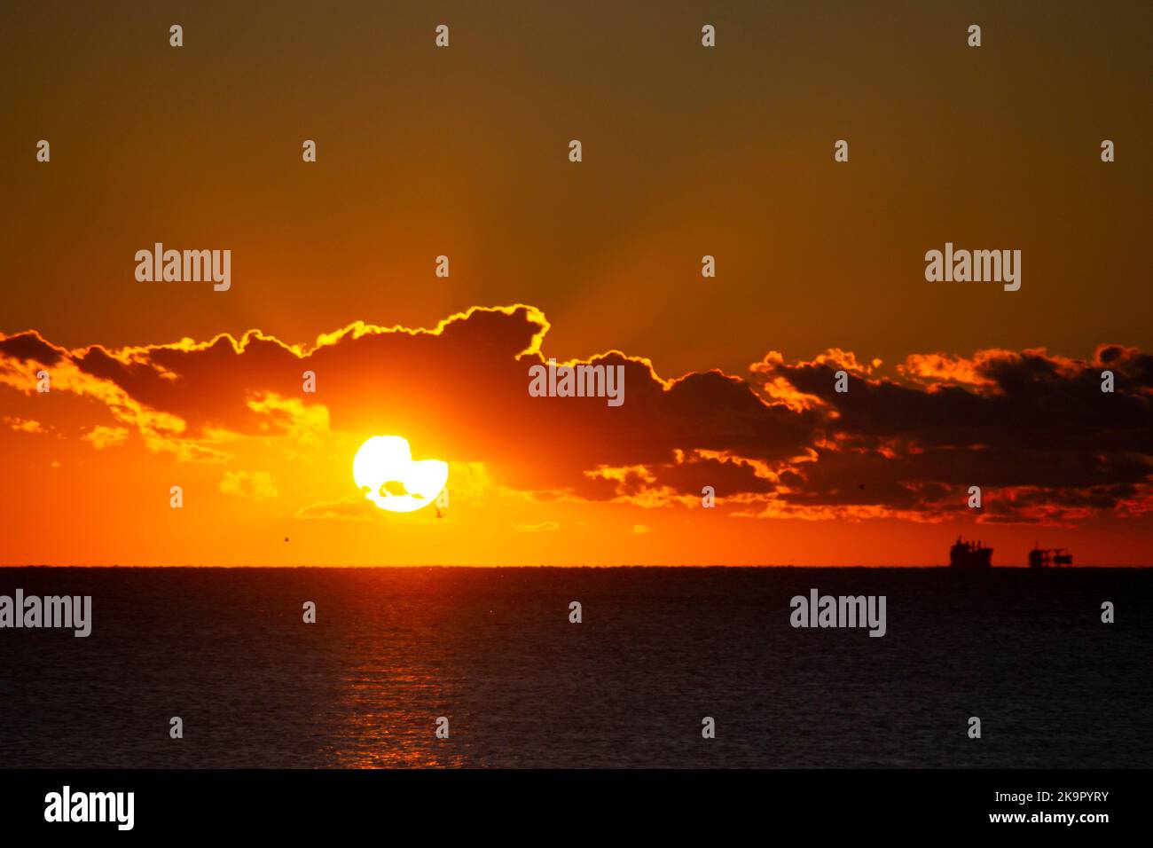 Le soleil de l'aube se couche derrière le nuage au-dessus de l'horizon marin à l'aube. Rayons de soleil. Lever du soleil sur la mer. Silhouettes noires de mer et de nuages. Ciel mer paysage. Seascape des nuages en mouvement rapide Banque D'Images