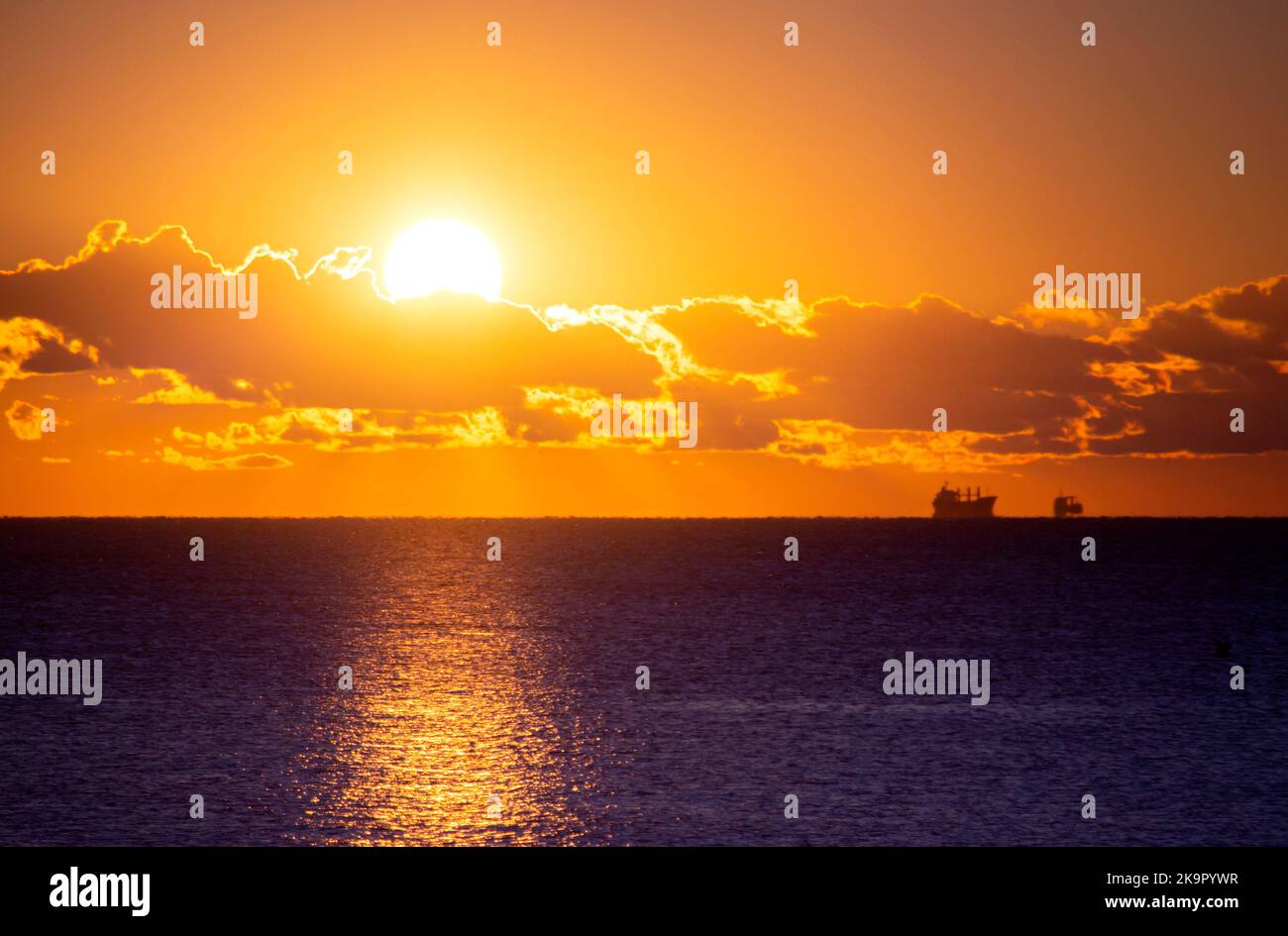 Soleil à l'aube, à l'aube, prenez le nuage au-dessus de l'horizon marin. Rayons de soleil rayons de soleil. Lever du soleil sur la mer. Deux silhouettes noires de camion-citerne de transport de grain sur la ligne d'horizon. Ciel mer paysage. Paysage marin Banque D'Images